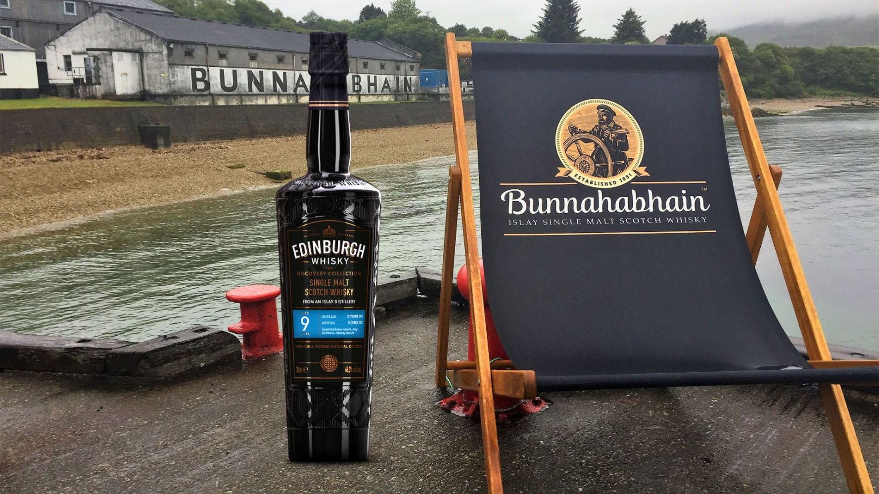 Bottle of Edinburgh Whisky beside a Bunnahabhain deck chair near a waterfront distillery.