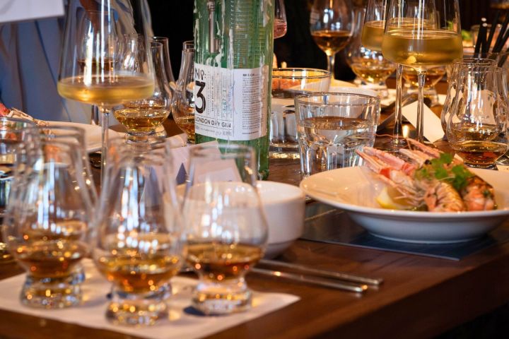 Table with whiskey glasses, a bottle, water glasses, and a dish of prawns.
