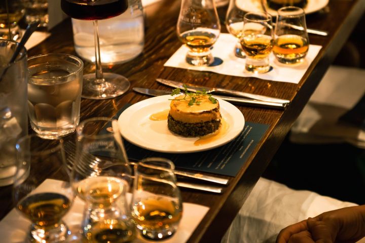 Table with whiskey glasses and a plated dish, surrounded by dim lighting.