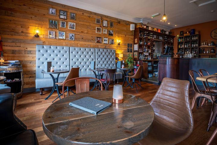 Cozy bar interior with wooden decor, tufted seating, and round tables.