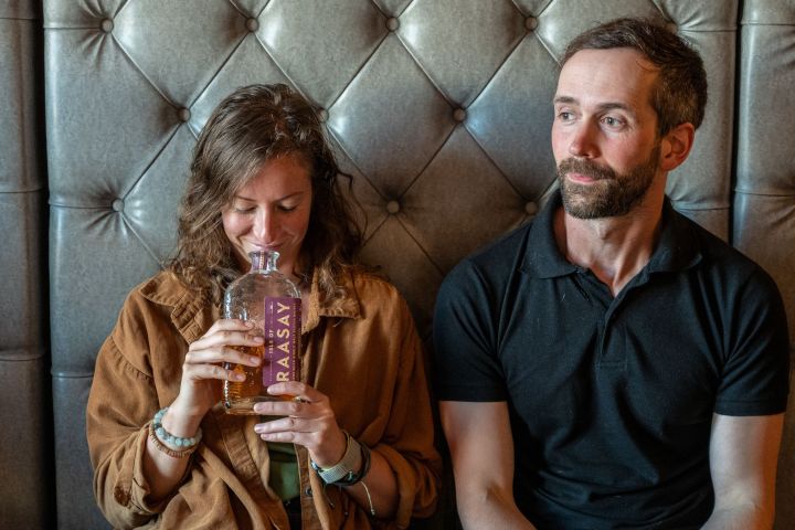 Woman smelling bottle, man sitting beside her on a tufted leather sofa.
