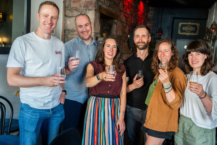 Six people in a bar holding glasses, smiling at the camera.