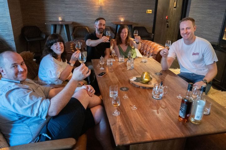 Group of five people toasting with drinks at a wooden table in a cozy room.