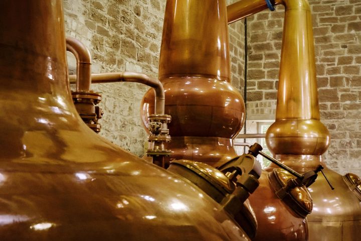 Row of large copper distillery tanks against a brick wall background.