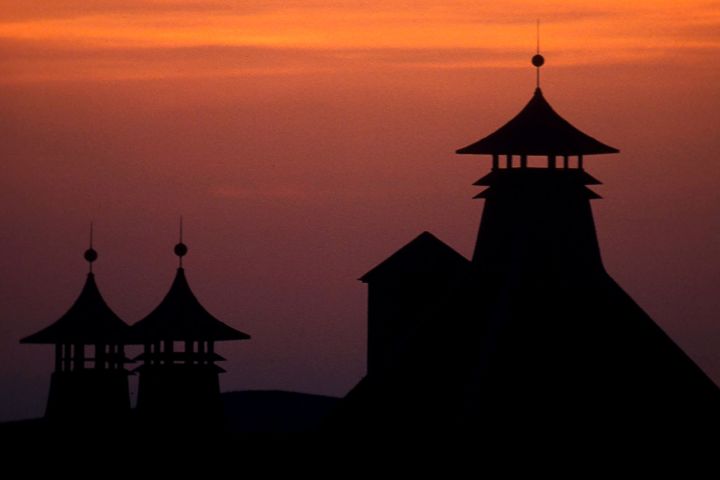 Silhouette of traditional pagoda-style roofs against an orange sunset sky.