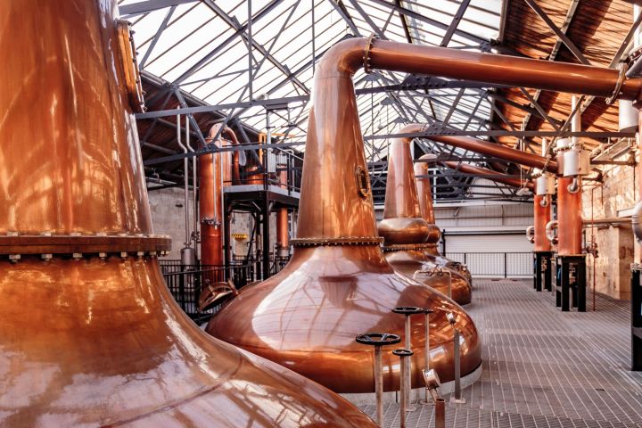Interior of a distillery with large copper stills and metal pipes.
