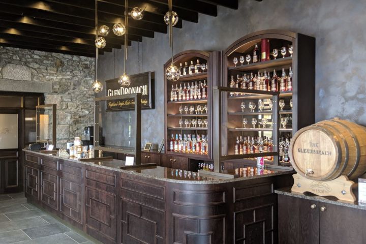 Whiskey bar with wooden decor, bottles on shelves, and a large barrel displayed.