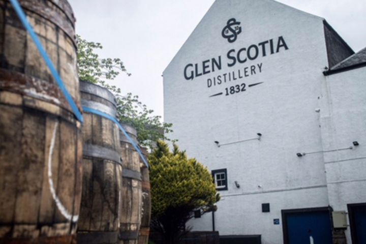 Barrels outside Glen Scotia Distillery, white building with trees and cloudy sky.