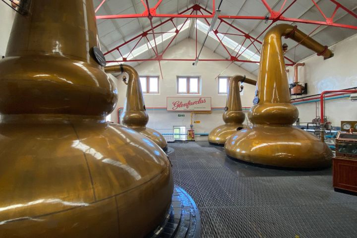 Interior of a distillery with large copper pot stills and a high ceiling with red beams.