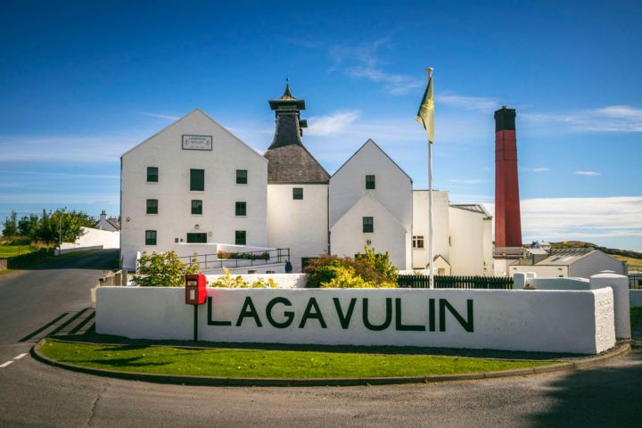 White distillery building with sign 'Lagavulin' under a blue sky.