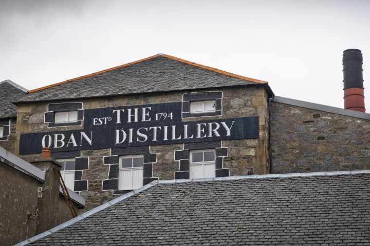 Stone building with a sign reading 'The Oban Distillery Est. 1794' on a cloudy day.