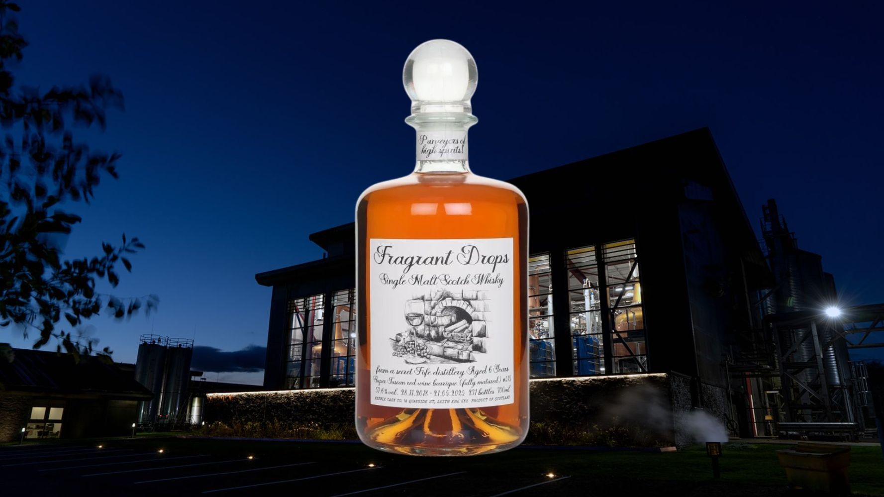 Glass bottle of whiskey in front of a distillery at night.