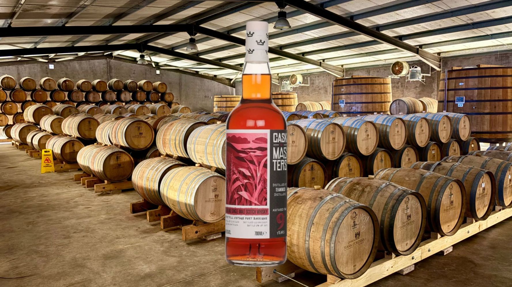 Whiskey bottle overlaid on a distillery with rows of wooden barrels.