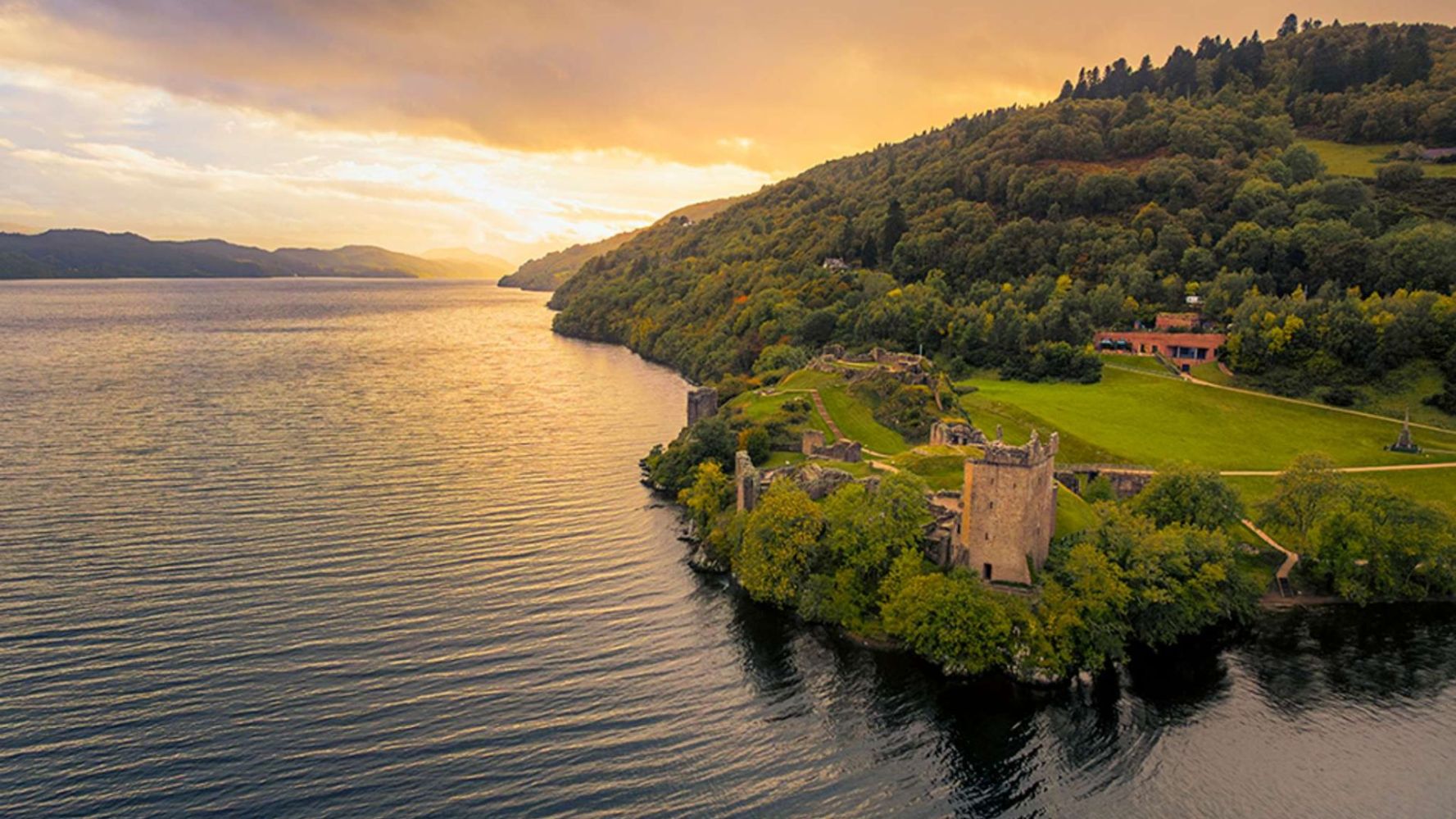 Aerial view of a lakeside castle surrounded by trees during sunset.