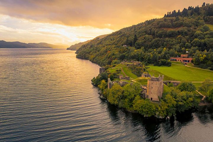 Aerial view of a lakeside castle surrounded by trees during sunset.
