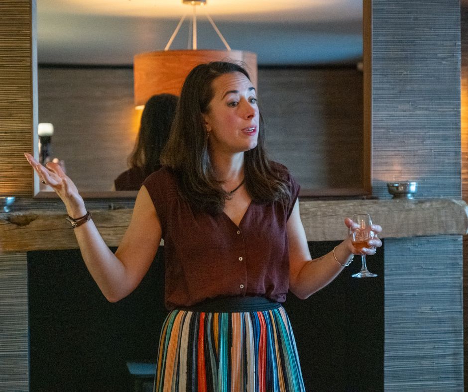 Woman speaking, gesturing with one hand, holding a drink in the other.