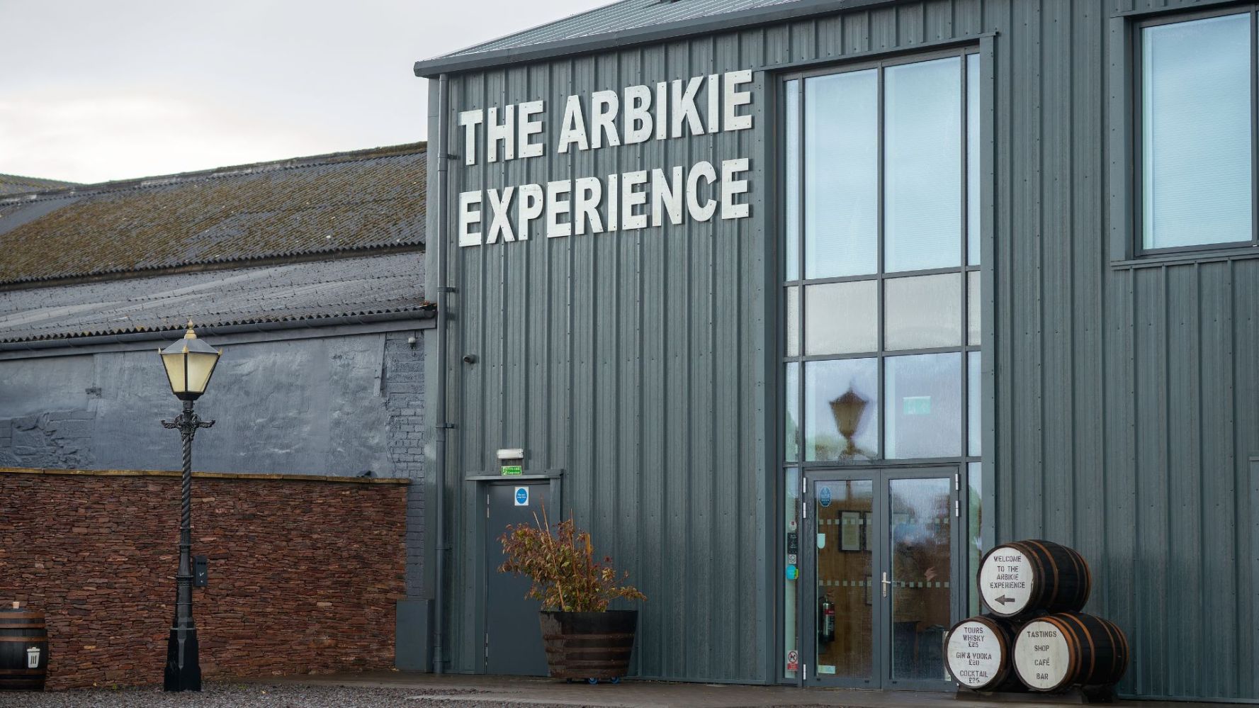 Grey building with 'The Arbikie Experience' sign and barrels by the entrance.