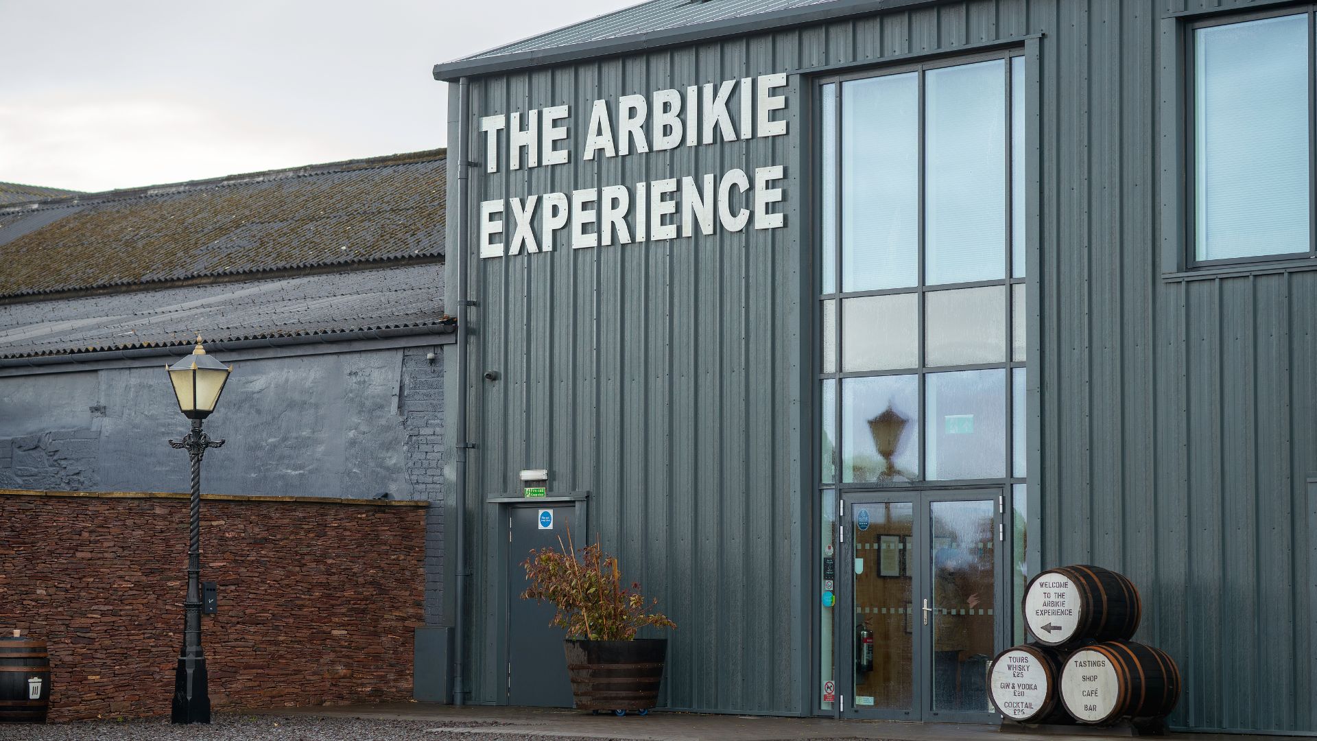 Grey building with 'The Arbikie Experience' sign and barrels by the entrance.