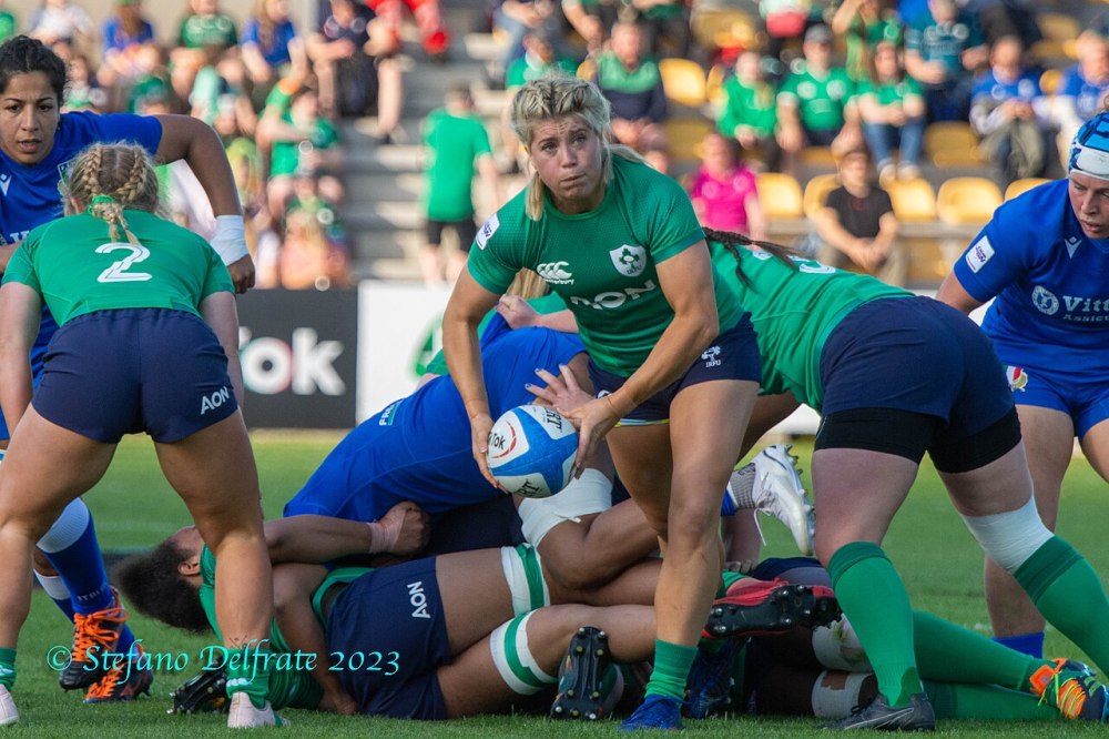 Female rugby player in green holds ball, surrounded by players.