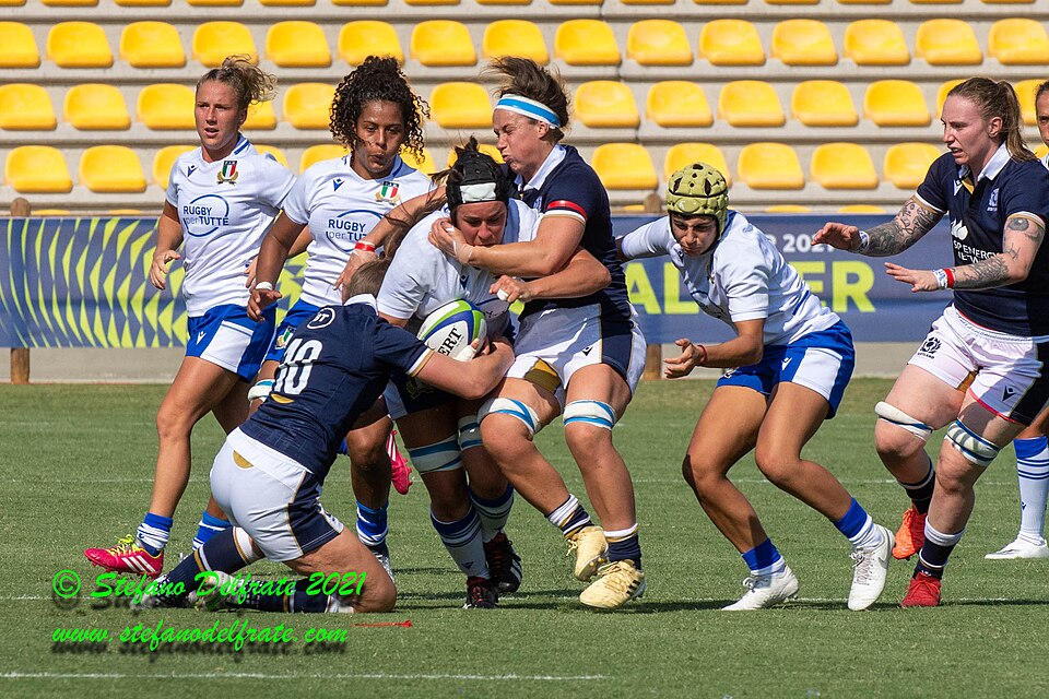 Women's rugby match with players in blue and white jerseys tackling and competing for the ball.