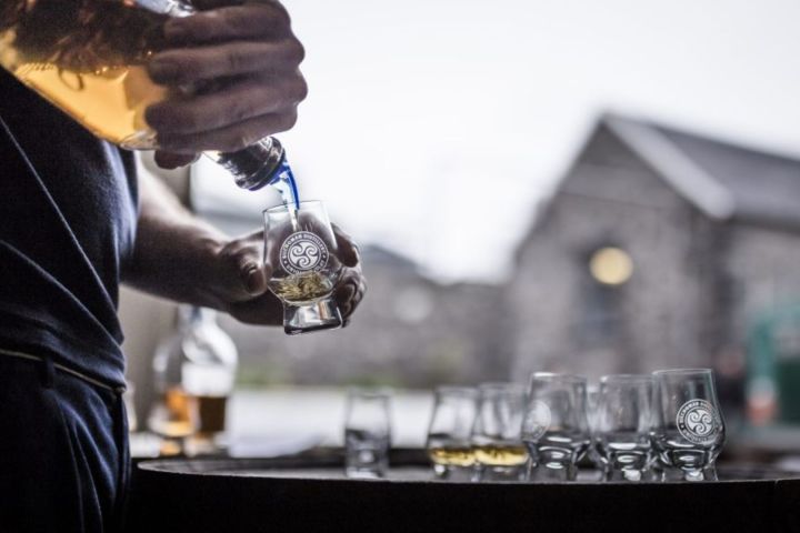 Person pouring whiskey into branded glass outdoors.
